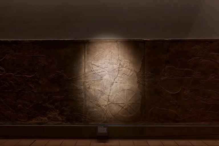 The Lion Hunt relief of Ashurbanipal in the British Museum, lit by a single spotlight before the projection begins