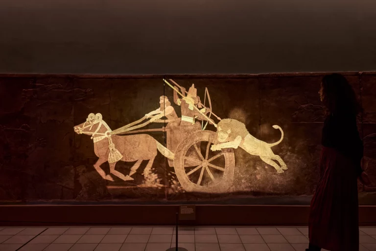The animated projection on the Assyrian relief: a glowing chariot and hunting lion brought to life across the carved stone