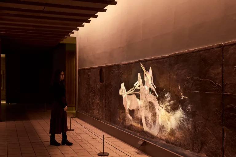 A visitor in silhouette watching the projection on the relief at the end of the gallery