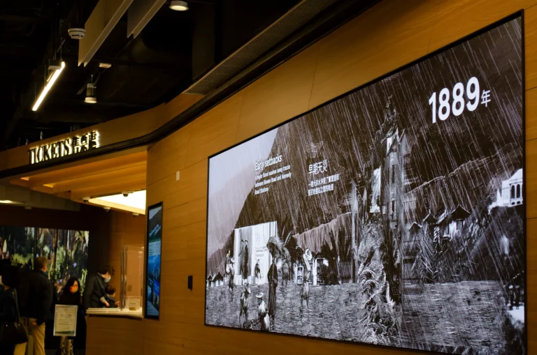 A large screen in the Peak Tram building showing a historic black and white photograph from 1889
