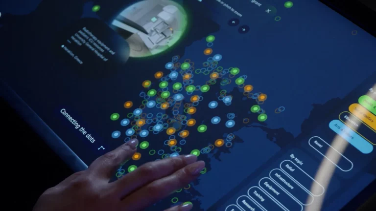 A hand selecting from a scatter of colourful data points on an interactive touchscreen table