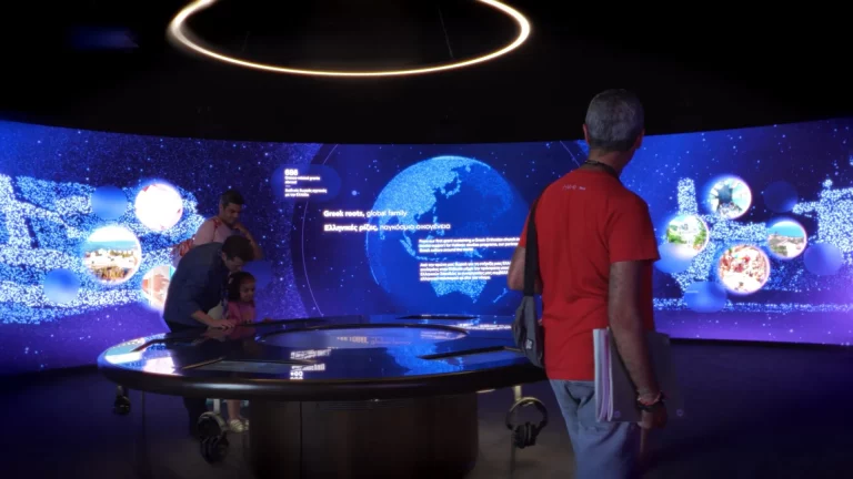 Visitors at a circular interactive table beneath a wide curved screen showing a glowing globe and data